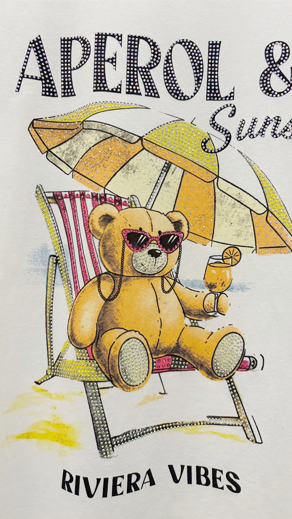 Close-up of rhinestone beach vibes graphic detail on t-shirt showing APEROL cartoon design